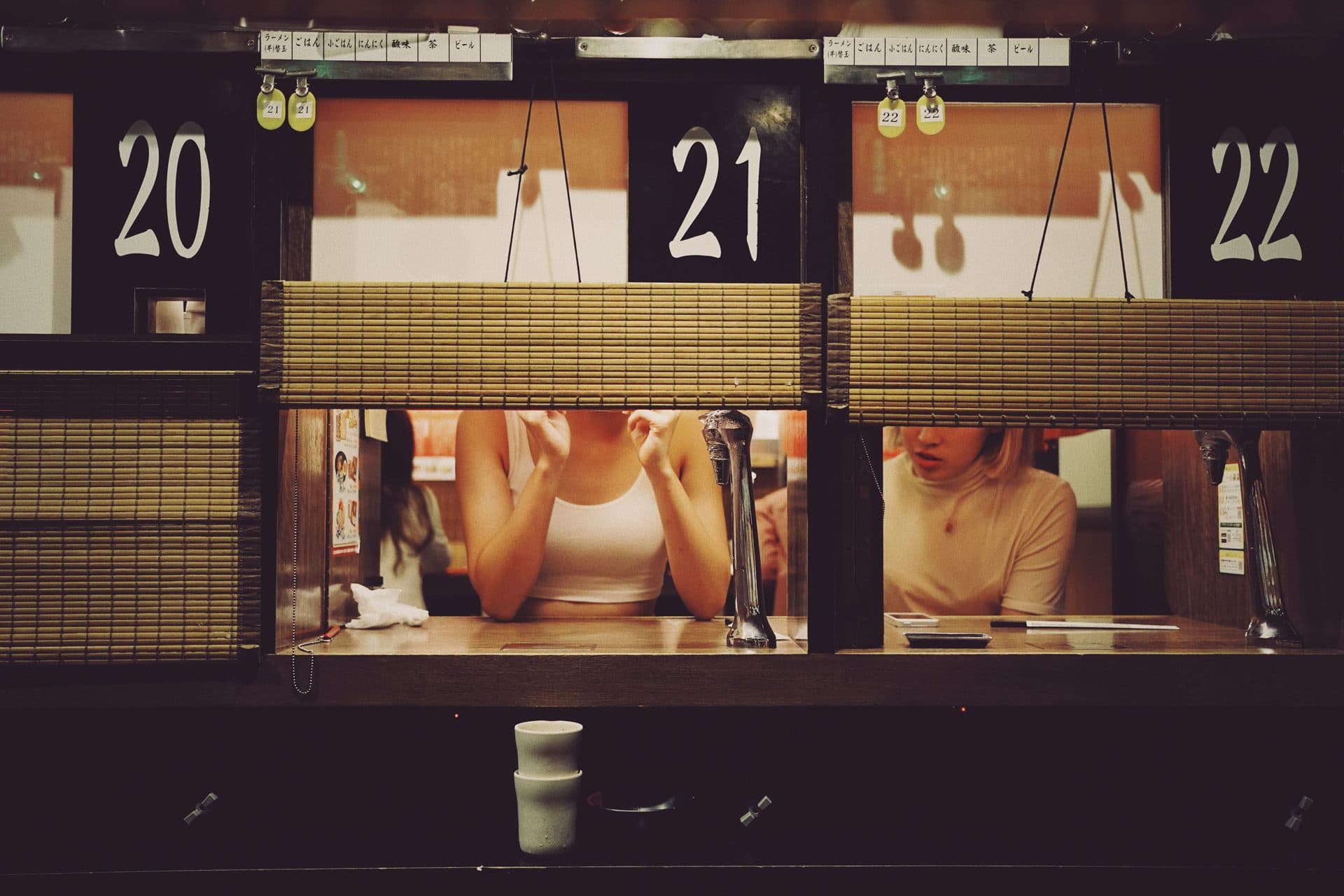 Diners seated at individual ramen booths in a Tokyo shop, bowls of noodles in front of them