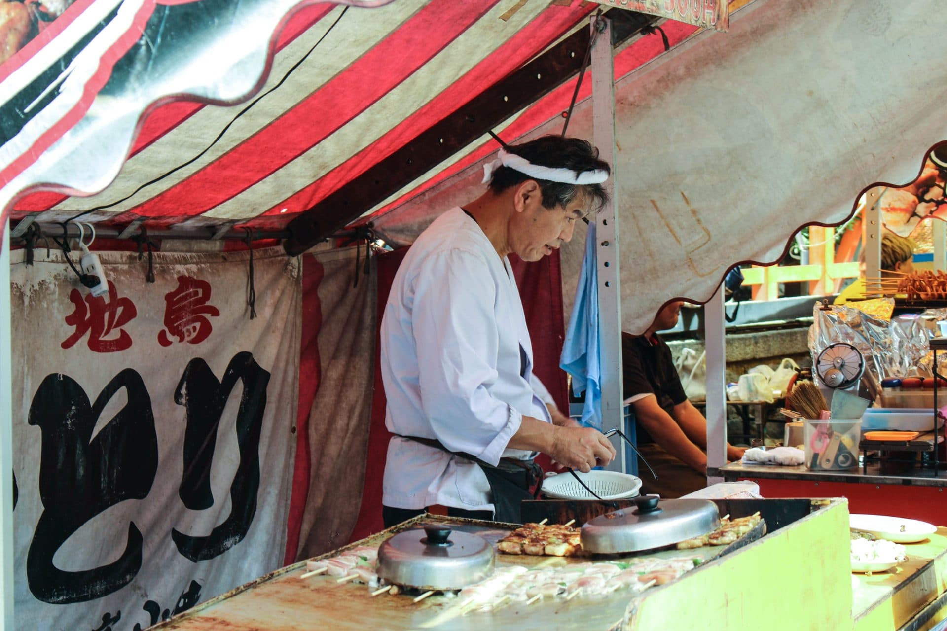 Man in white robe cooking on market stall
