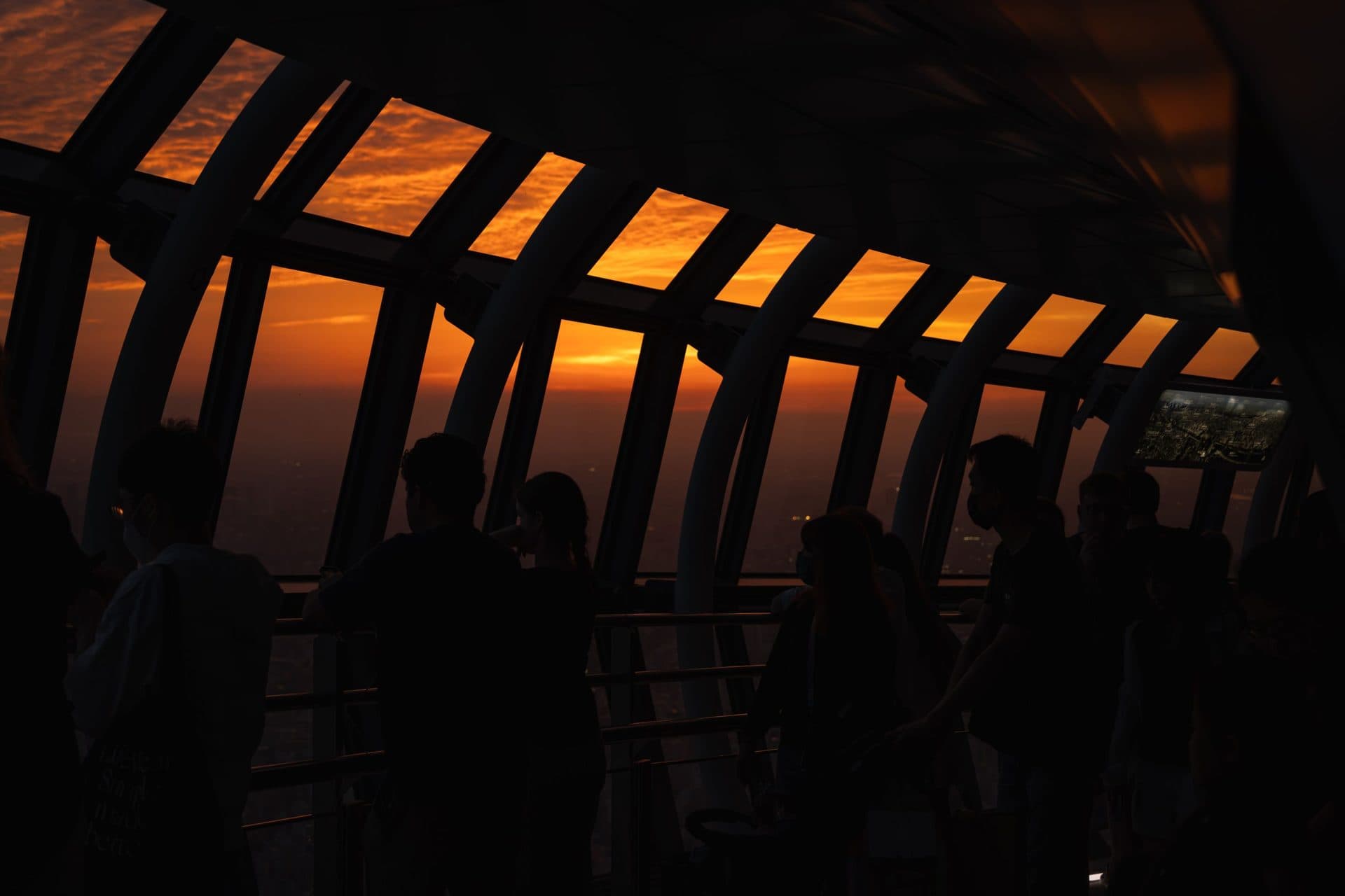 Silhouetted visitors observe a vibrant sunset from a rooftop observation deck in Tokyo