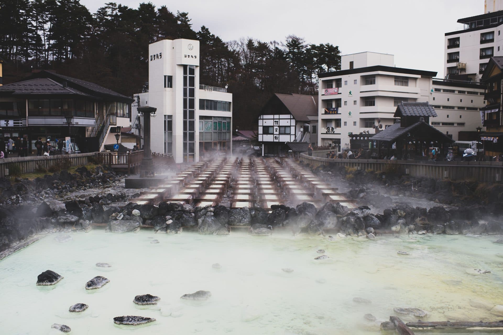 A hot spring town in the mountains near Tokyo with steam rising from mineral-rich waters, surrounded by traditional inns