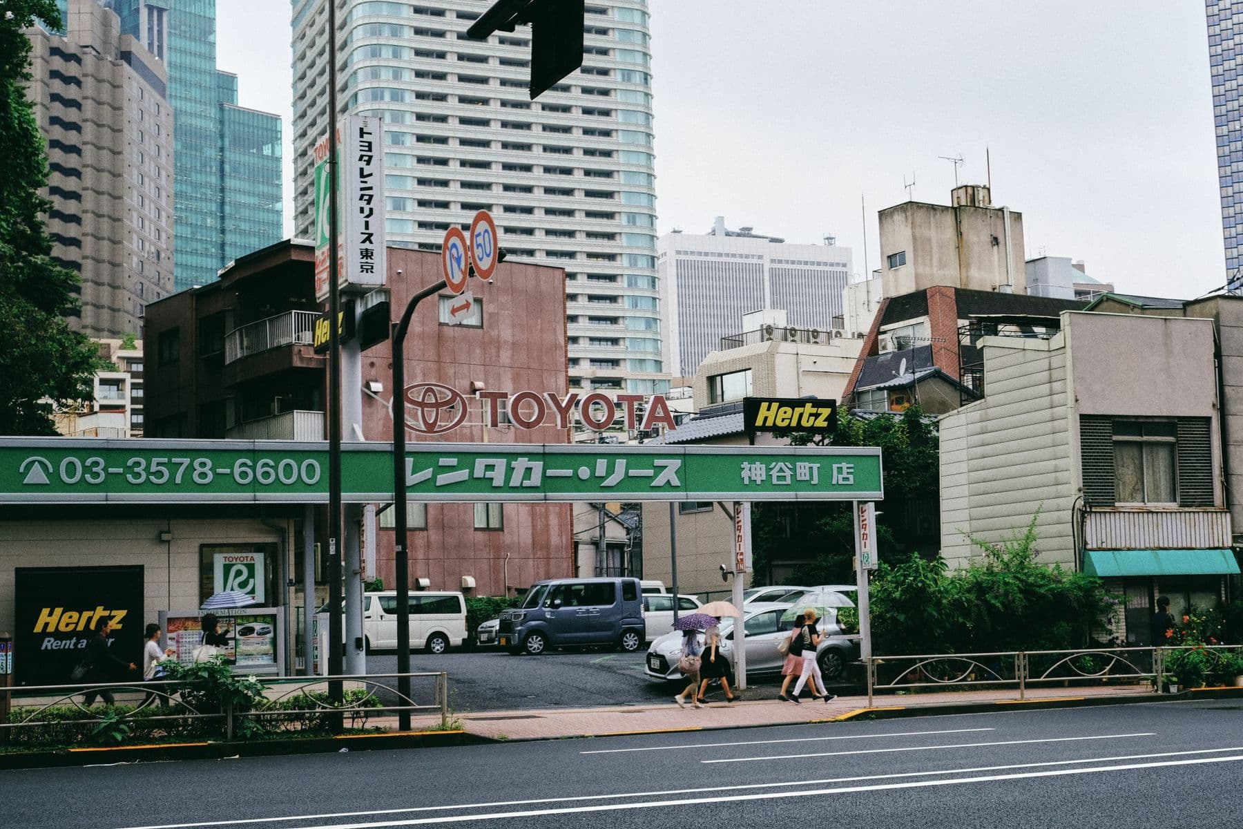 Street view featuring a car rental sign with city buildings in the background
