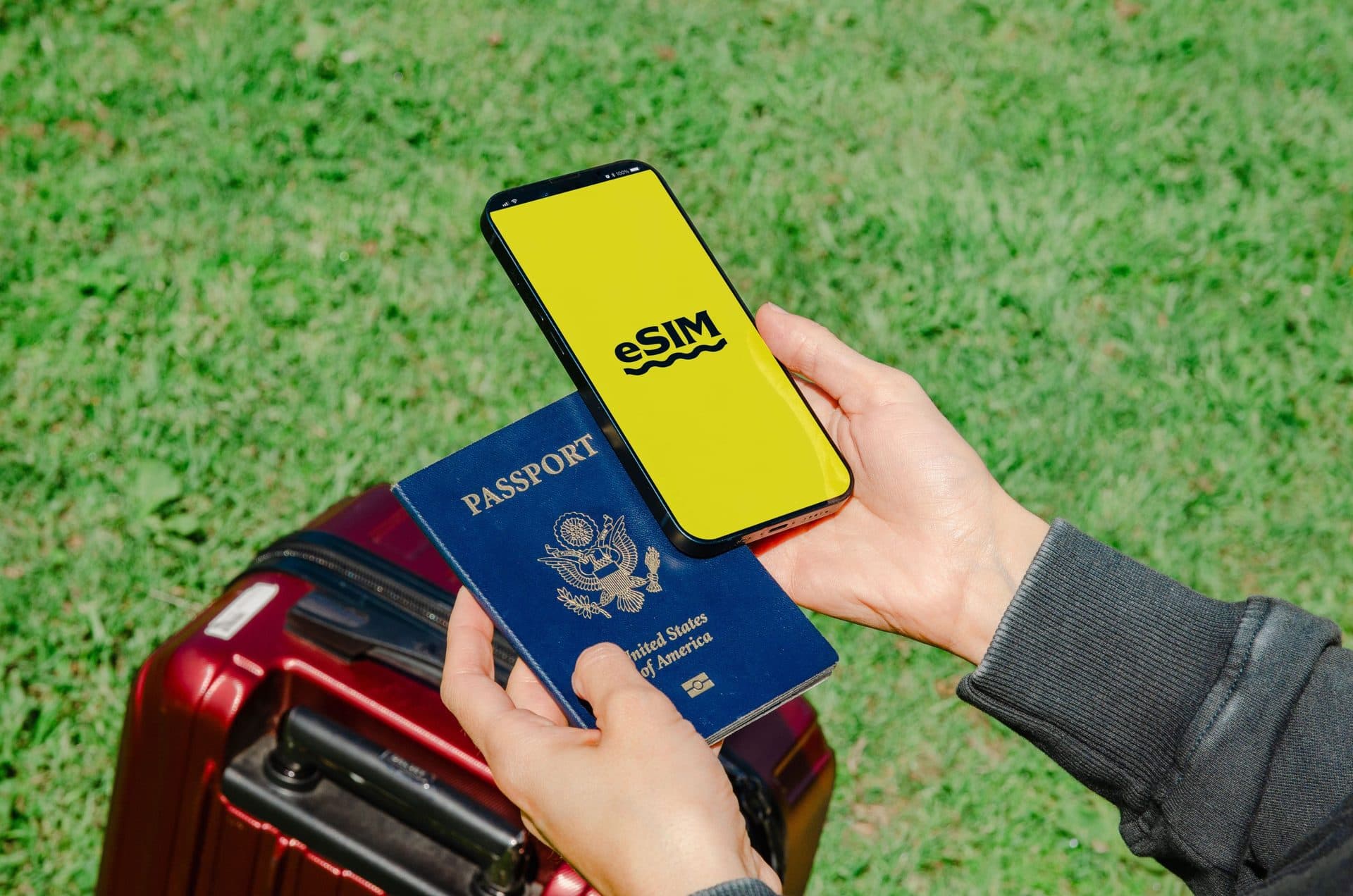 Hands holding a smartphone with eSIM setup and a passport near luggage