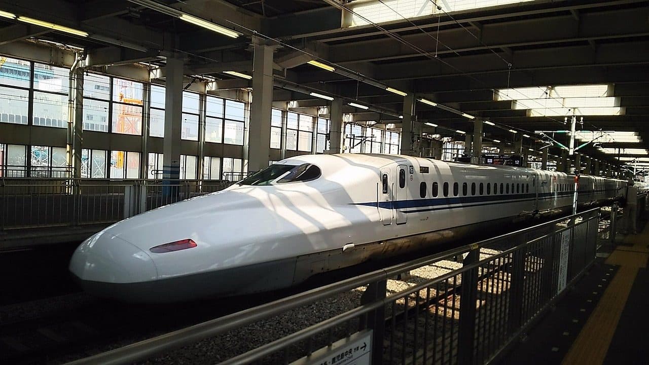 A white N700-series Shinkansen bullet train with a blue stripe waiting at a covered station platform on the Sanyo line