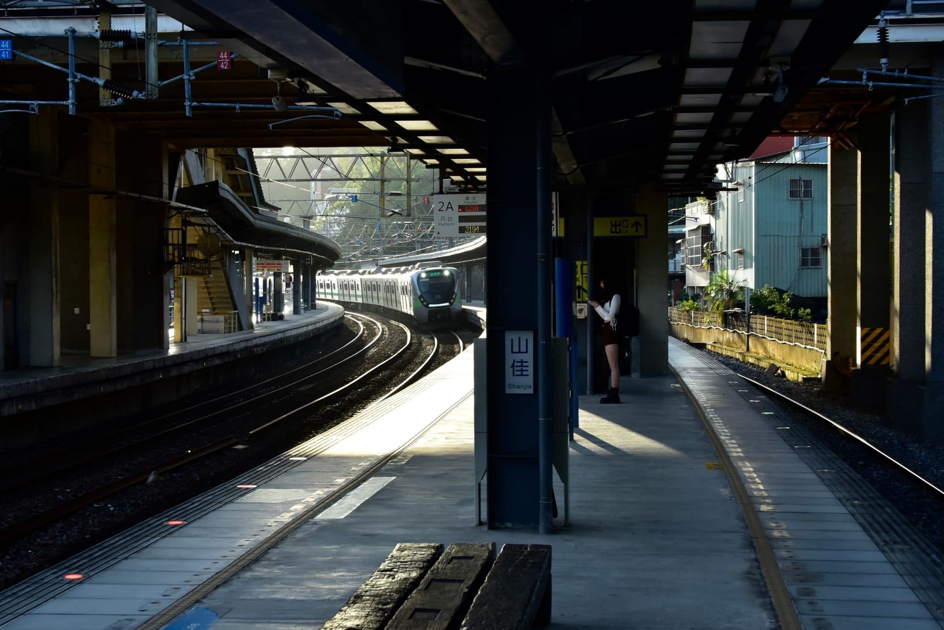 Empty Japanese train station platform under evening light with an arriving train and a person waiting