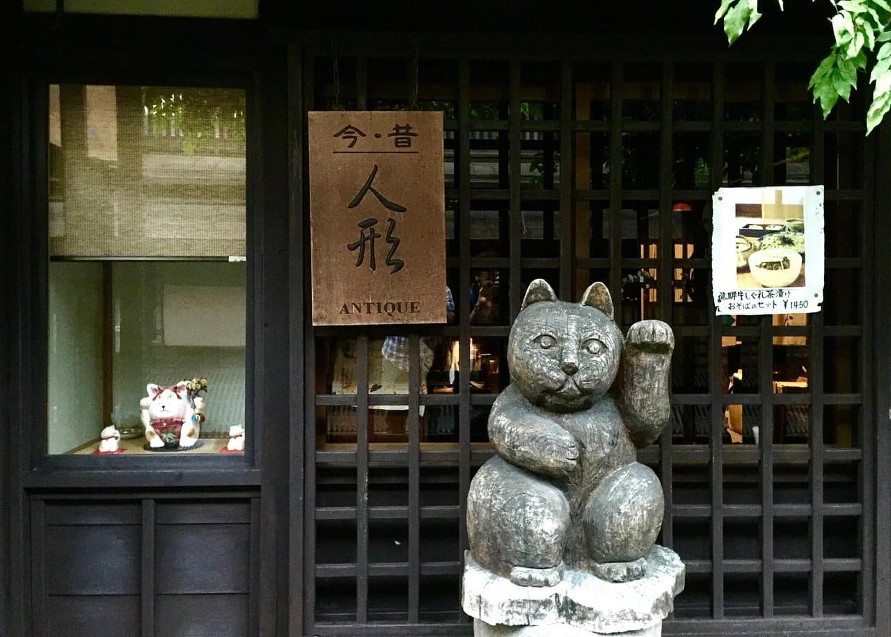 A dark wooden lattice shopfront in Takayama's old town with a carved wooden beckoning-cat statue and an antique doll shop sign