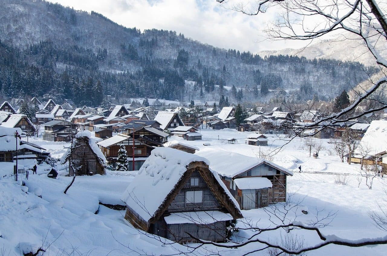 Thatched gassho-zukuri farmhouses in Shirakawa-go buried in deep snow, with snow-covered forested mountains behind