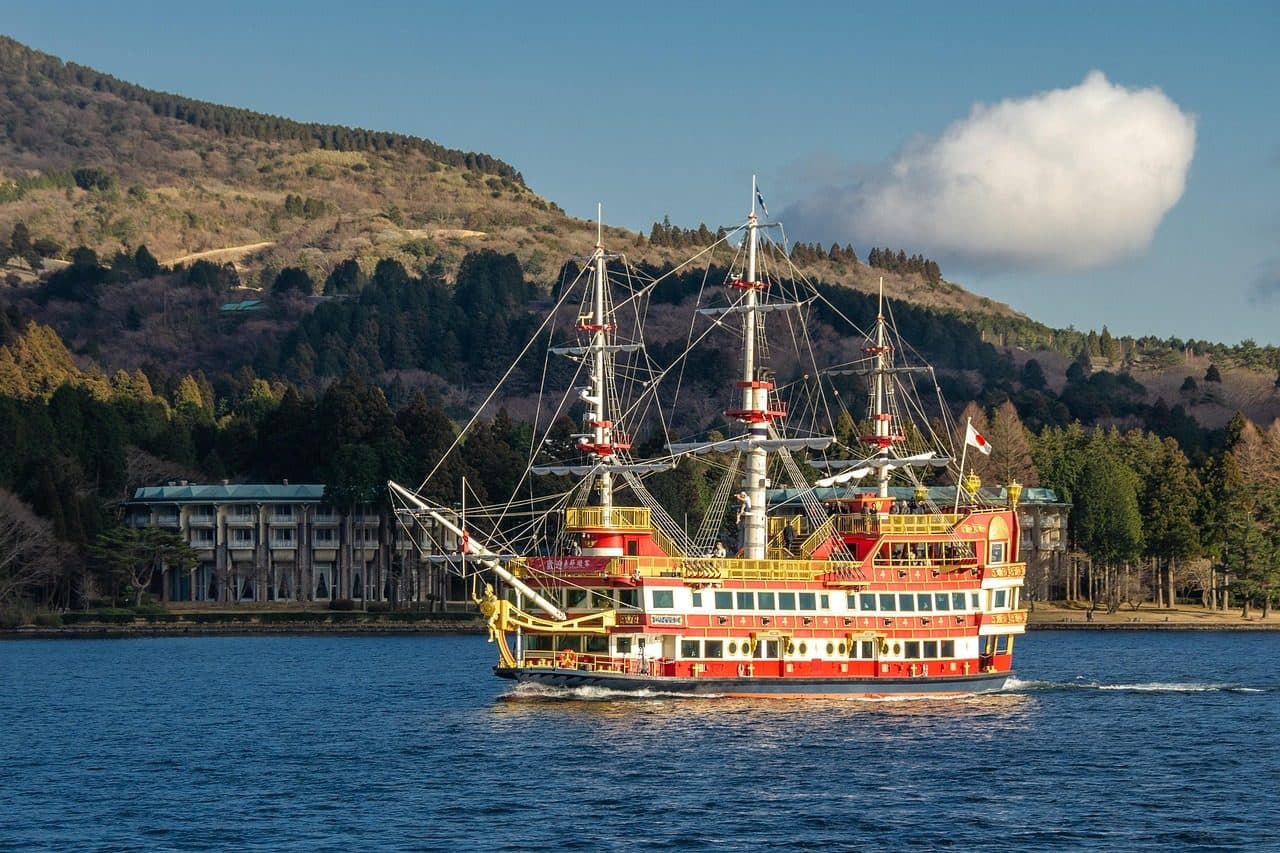 A red and gold pirate-ship style sightseeing cruise boat sailing on Lake Ashi in Hakone, with wooded hills behind